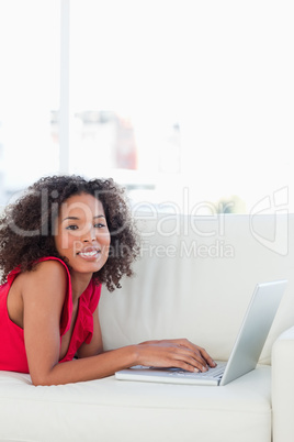 Woman looking forward, smiling and using her laptop on the couch