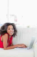 Woman looking forward, smiling and using her laptop on the couch