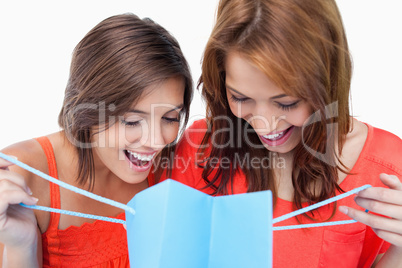 Two teenage girls looking at a their purchases against a white b