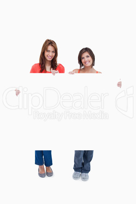 Two smiling teenage girls holding a blank poster against a white