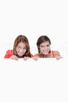 Teenage girls smiling while holding a blank poster and hiding be