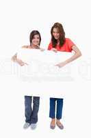 Smiling teenage girls standing upright behind a blank poster whi