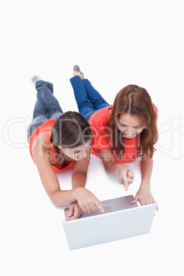 Two smiling teenagers pointing their fingers on the laptop scree