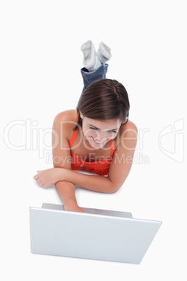 Smart teenage girl lying down in front of a laptop with legs cro