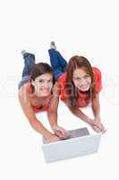 Two attractive teenage girls lying down with a laptop while look