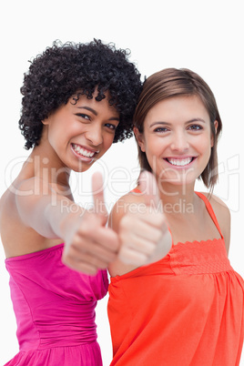 Smiling teenage girls proudly showing their thumbs up against a