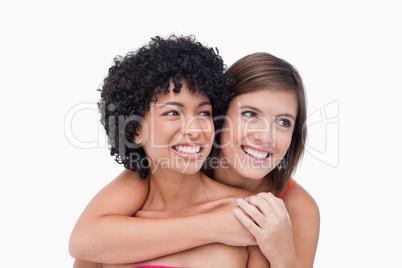 Smiling teenagers looking on the side while hugging each other