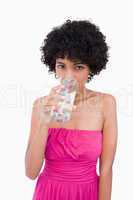 Young woman looking straight ahead while drinking a glass of wat