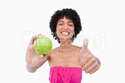 Smiling teenager holding a green apple and putting her thumbs up