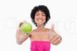 Smiling teenager holding a green apple and putting her thumbs up