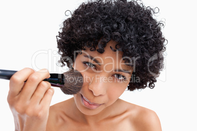 Young woman applying natural blush on her face