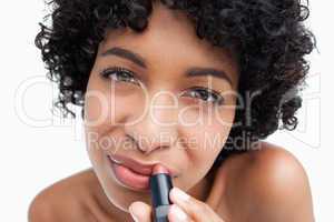 Young brunette applying lipstick against a white background
