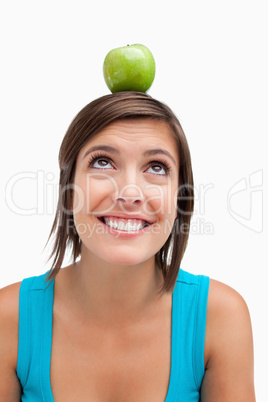 Smiling teenage girl trying to look at a green apple placed on h