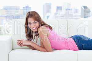 Smiling young woman lying on a sofa while looking at the camera