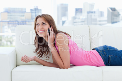 Young smiling woman lying on a sofa while talking on the phone