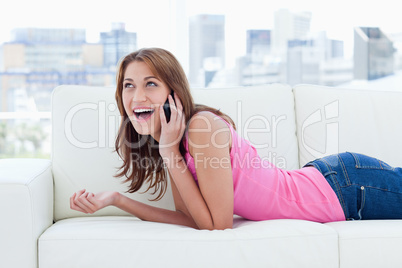 Young woman lying on a sofa while looking up and talking on phon