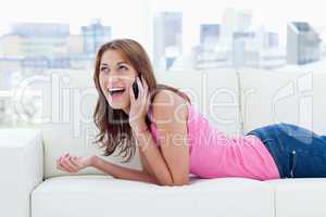 Young woman lying on a sofa while looking up and talking on phon