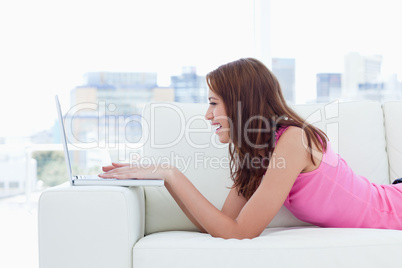 Young woman writing on a laptop placed on the arm of the sofa