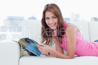 Smiling young woman reading a magazine on the sofa while looking