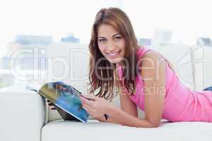 Smiling young woman reading a magazine on the sofa while looking