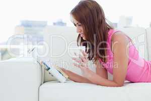 Young woman holding a cup of coffee while reading a magazine