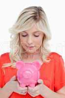 Young woman looking at a piggy bank held by her hands