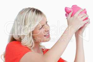 Fair-haired woman shaking a pink piggy bank