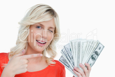 Woman winking an eye while pointing her finger on dollar notes