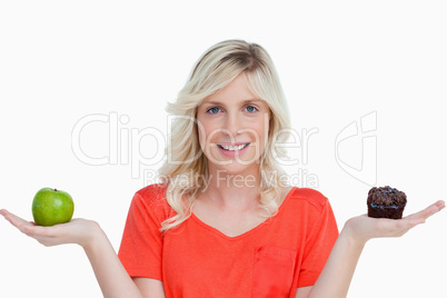 Woman beaming while holding a chocolate muffin and a green apple