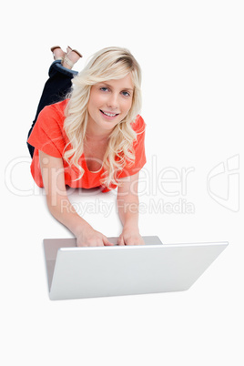 Smiling attractive woman using her laptop while lying on the flo