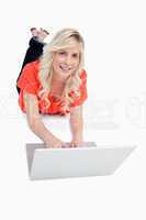 Smiling attractive woman using her laptop while lying on the flo
