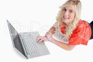 Smiling young woman using her laptop while lying down