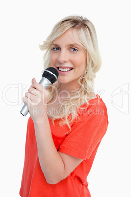 Young blonde woman smiling while singing into a microphone