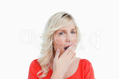 Young blonde woman yawning and covering her mouth with her hand