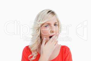 Young blonde woman yawning and covering her mouth with her hand