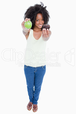 Smiling young woman holding an apple in one hand and a muffin in