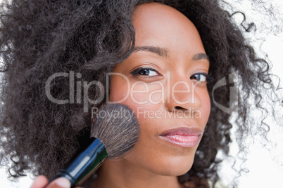 Young serious woman applying blush with powder brush