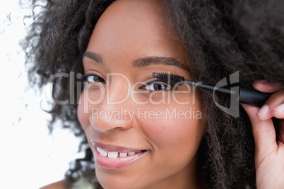 Young smiling woman applying mascara on her eyelashes