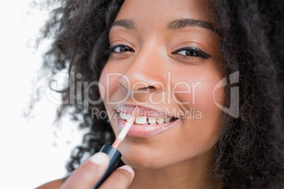 Young smiling woman making-up while using a lip gloss applicator