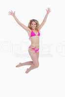 Smiling blonde woman jumping while raising her arms