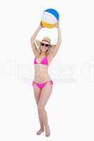Smiling teenager in a pink swimsuit raising a beach ball above h