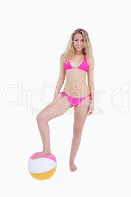 Smiling attractive teenager placing her foot on a beach ball