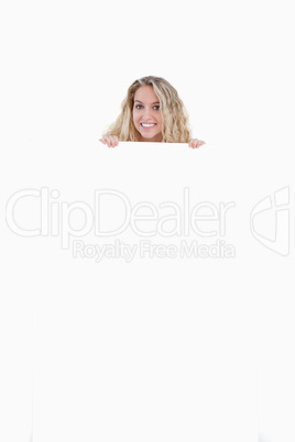 Smiling young woman hiding her body behind a blank poster
