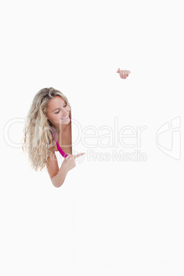 Young smiling woman pointing her finger at a blank poster
