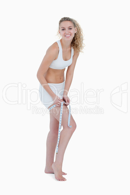 Smiling young woman measuring her thigh with a measure tape