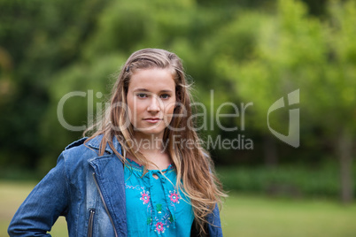 Serious teenage girl standing upright in a park