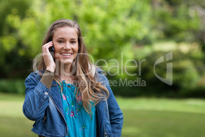 Young smiling girl talking on the phone while standing in a park