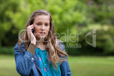 Young serious woman using her mobile phone while standing in a p