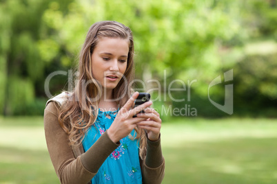 Serious teenage girl sending a text while standing in a park