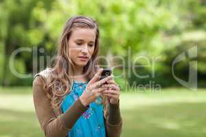 Serious teenage girl sending a text while standing in a park